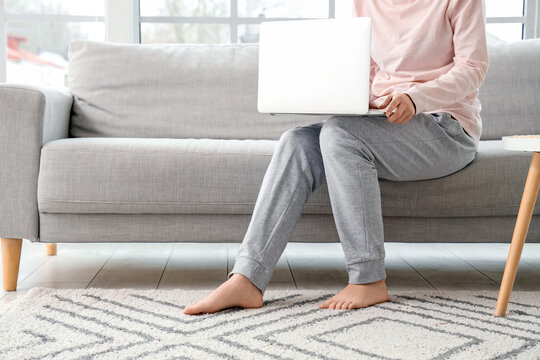 Barefoot woman using laptop on sofa at home