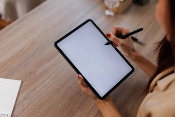 Mockup image of business woman sitting on the wooden table using stylus pen and digital tablet with blank white desktop screen.
