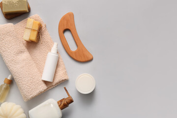 Composition with wooden guasha body massage tool, bottles of cosmetic products and towel on grey background