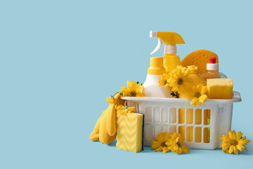 Basket with set of cleaning supplies and spring flowers on blue background