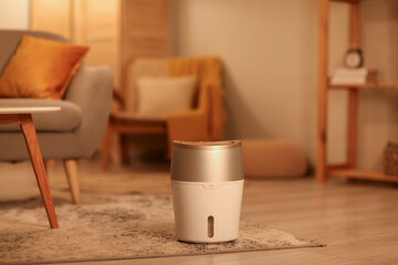 Modern humidifier near sofa on floor in living room at evening