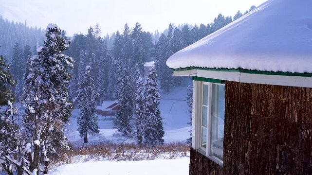 panning up reveal from fresh snow on ground to wooden cabin home house, resort with himalaya mountain covered in pine deodar trees in the background in Gulmarg Srinagar Kashmir