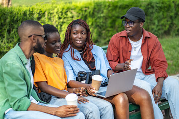Diverse group of students in park with laptops, sipping coffee, chat and study. African group preparing for exams, surfing internet, social time and study, university teamwork on break, freelance job