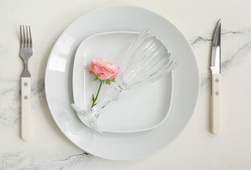 Composition with white clean plates, flower, cutlery and glass on marble table