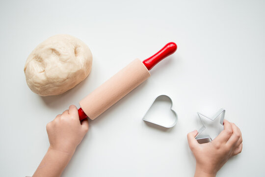 Child hands using rolling pin and cookie cutters for baking on white surface