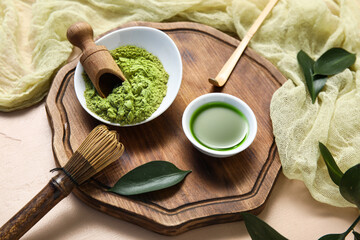 Bowls of matcha tea and powder with chasen on beige background