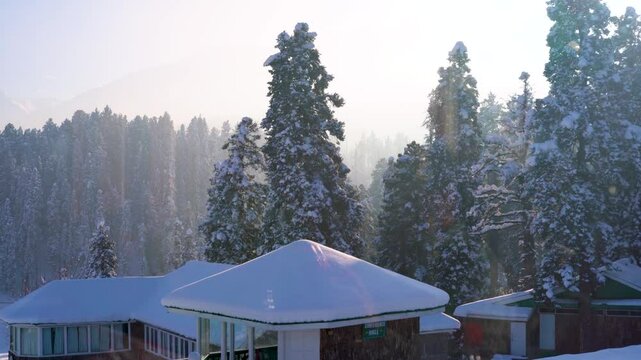 Locked shot showing wooden cabins covered in snow with pine deodar trees surrounding it and the Himalaya mountains peeking out of the fog in the distance in Gulmarg Srinagar Kashmir