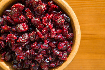 Dried cranberries in a wooden bowl on a wooden table. Top view.