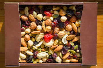 Mix of nuts and dried fruits in a box on wooden background. Top view.