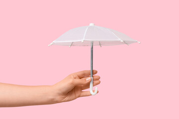 Female hand with mini umbrella on pink background