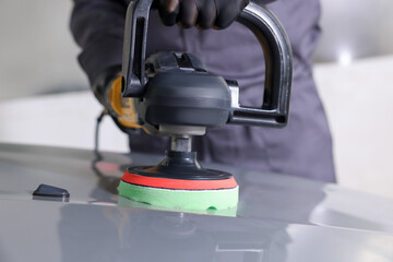 Man polishing car hood with orbital polisher indoors, closeup