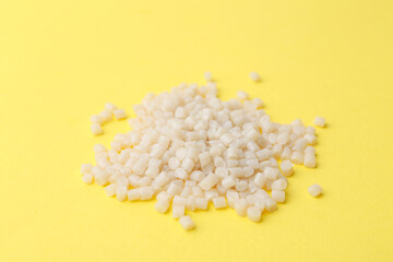 Pile of plastic granules on yellow background, closeup
