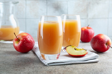 Refreshing apple juice in glasses and fruits on grey textured table, closeup