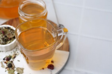 Delicious herbal tea with honey and dry leaves on white tiled table, closeup. Space for text