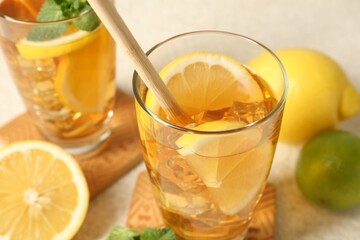 Refreshing iced tea with drinking straw, lemon and lime on light table, closeup