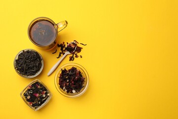Aromatic tea and dried leaves on yellow background, flat lay. Space for text