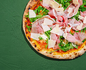 Freshly made pizza topped with prosciutto and arugula on a table