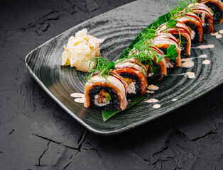 Sushi rolls served on a dark plate with garnishes and sauce