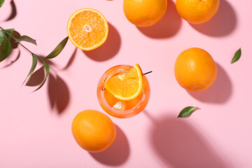 Glass of Aperol spritz cocktail with oranges and leaves on pink background