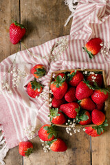Fresh strawberries in a wooden basket with flowers on a rustic table.