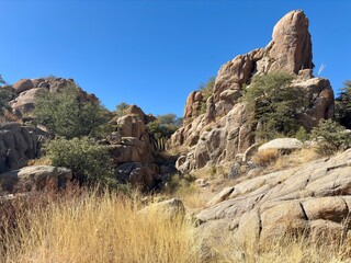 Rugged rock formations with dry grass and shrubs under blue sky
