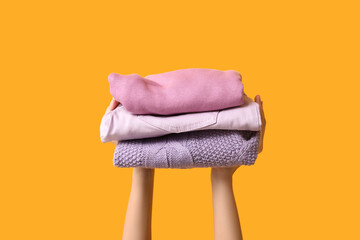 Female hands with stack of warm clothes on yellow background