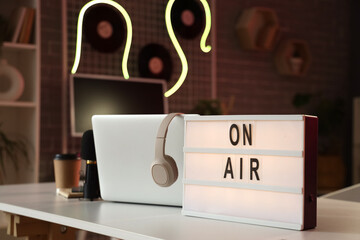 Board with text ON AIR and laptop on table in podcaster's studio, closeup