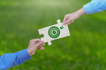 Green business partnership and teamwork concept. Two hands connect a puzzle piece with a green...