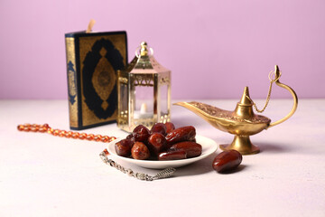 Dates, Koran and Aladdin lamp on white table against lilac background. Ramadan celebration