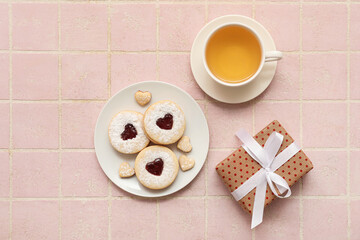 Plate with sweet cookies, cup of tea and gift for Valentine's day celebration on color tile background