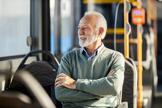 Portrait of an old trendy man in smart casual sitting in pubic bus with arms crossed and looking trough the window.