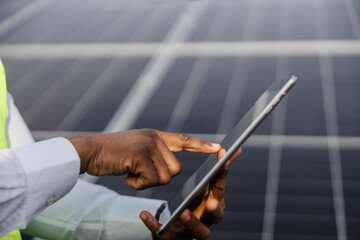 Close up of innovative interracial engineer's hand scrolling on tablet with solar panels in background.