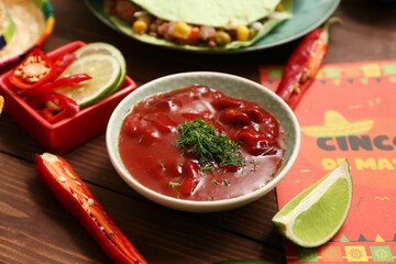 Bowl with traditional Mexican salsa sauce and chili peppers on wooden background, closeup. Cinco de Mayo (Fifth of May) celebration