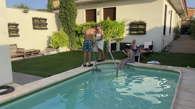 Middle-aged mother and teenage son spending a calm summer afternoon in a private backyard pool area, relaxing and enjoying quiet family moments in a sunny residential outdoor environment in Spain