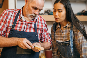 Two carpenters in plaid shirts carefully carve wood on a workbench in a workshop, using specialized tools. The scene highlights their precision and skill, embodying the craftsmanship of carpentry work