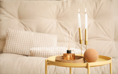 Reed diffuser with burning candles on table in living room, closeup