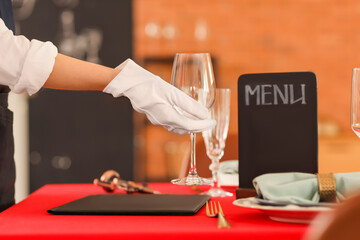 Young waitress putting glass on table in restaurant, closeup