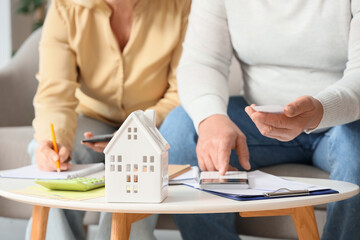 House figure on table against senior couple calculating utility bills at home, closeup