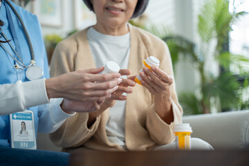 Asian Caregiver nurse showing pills bottle drugs and consultant to senior woman patient.Doctor or Nurse with physician visit elderly mature female patient consult medicine dosage in livingroom at home