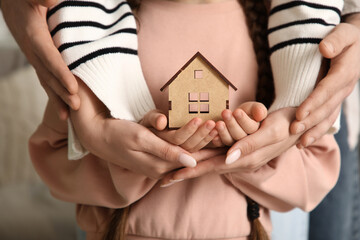 Couple with adopted girl holding wooden house at home, closeup
