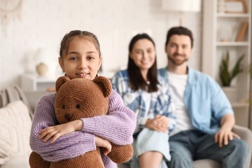 Happy adopted girl with toy bear and parents at home