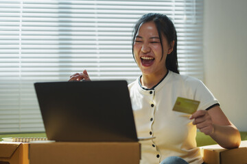 Asian woman entrepreneur is happy after making online sales via laptop and credit card