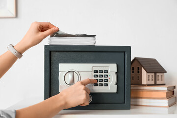 Woman with money opening safe on shelf at home, closeup