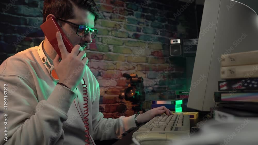 Aufkleber video editor from 1990's making phone call on landline telephone in front of computer and vhs casset