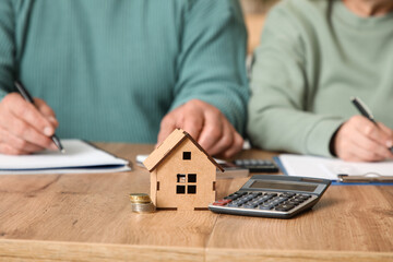 Senior couple with house figure calculating utility bills on table in kitchen, closeup