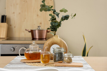 Vase with eucalyptus branches, teapot and dry tea on dining table in kitchen