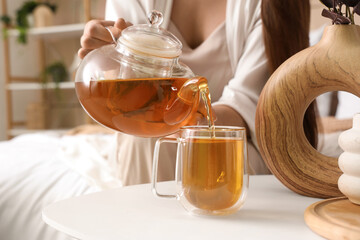 Young woman pouring green tea into glass cup on table in bedroom, closeup