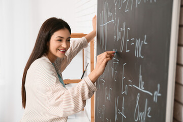 Female inventor writing mathematical formulas on chalkboard in workshop