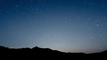 A movement of stars in the night sky with the view of mountains..