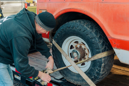A hardworking man in workwear secures a ratchet strap on a trailer